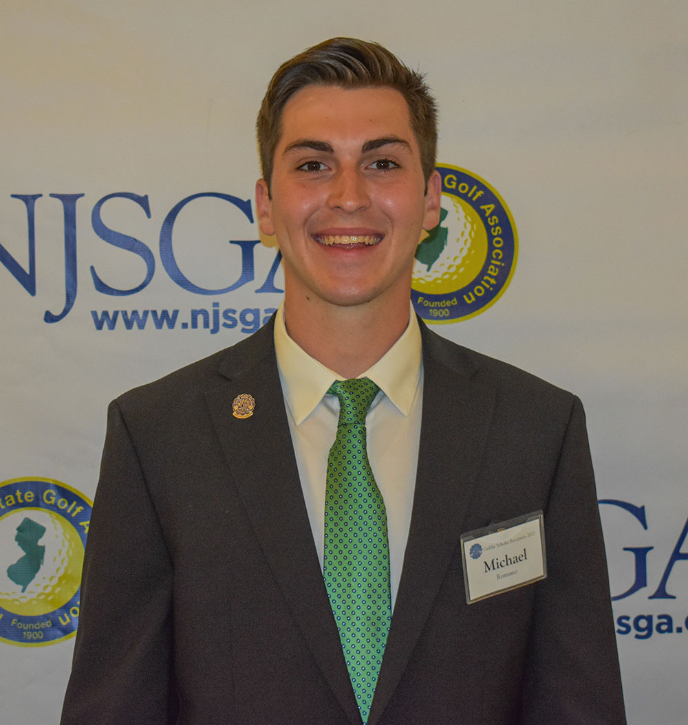 Michael Romano wearing a dark suit and green tie, standing in front of a backdrop with the 'NJSGA' logo.