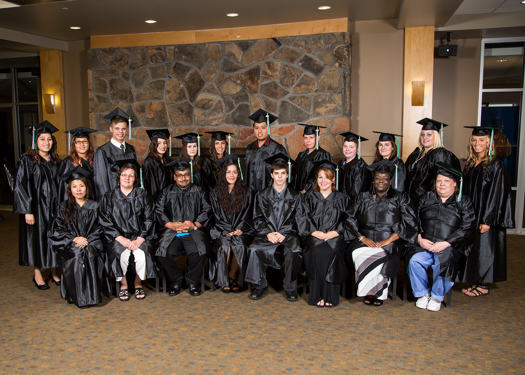 students dressed in graduation cap and gowns standing in two rows smiling for posed photo