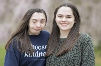 Twin sisters, including one wearing a blue sweatshirt that says Choose Kindness, are standing in front of a blurred background. Marywood Students to Give Kindness Presentation in San Diego