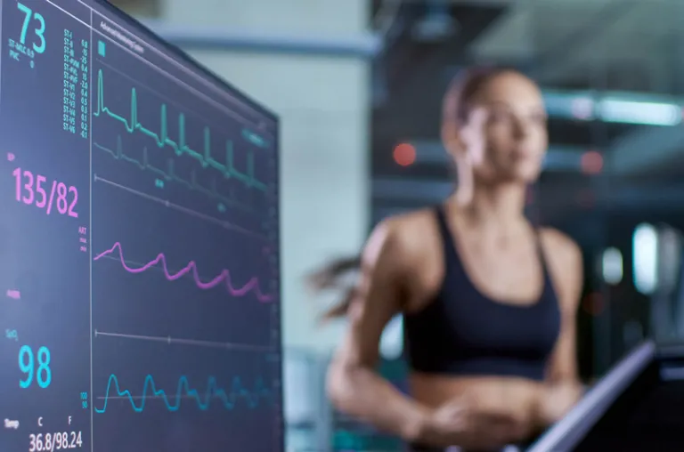 An athlete running on a treadmill next to a screen displaying their vitals