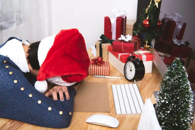 A person wearing a santa hat laying their head down on a desk. Harmony for the Holidays