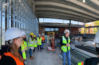 Students in hard hats and reflective vests are pictured at the construction site of a campus facility, the Pascucci Health Sciences Pavilion.