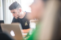 focused on guy staring intently at computer screen with blurred images of other students and laptops in front of him