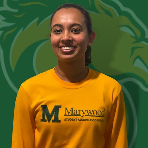 Young woman smiling wearing a yellow marywood shirt in front of the marywood pacer logo backdrop