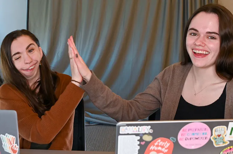 two female student high-five at laptops