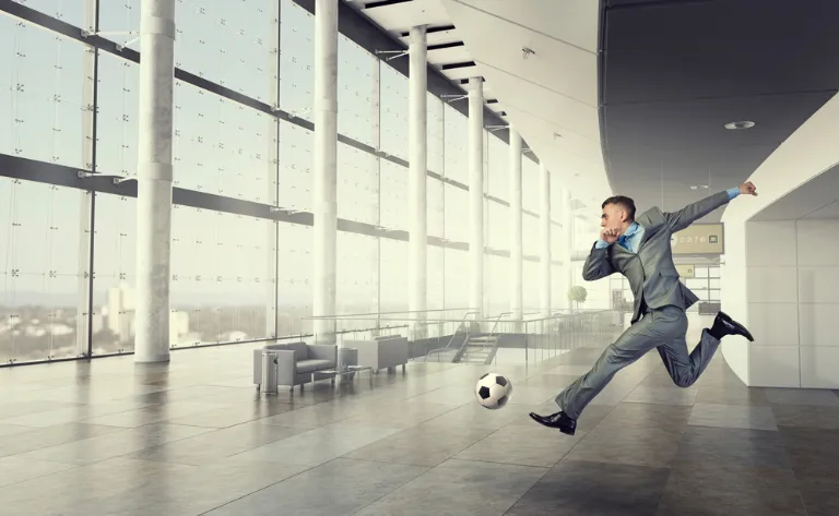 Businessman kicking a a soccer ball in an office setting.