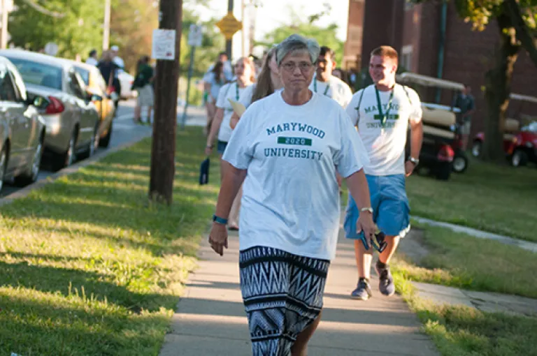 Sister Mary Persico walk on sidewalk toward camera with students