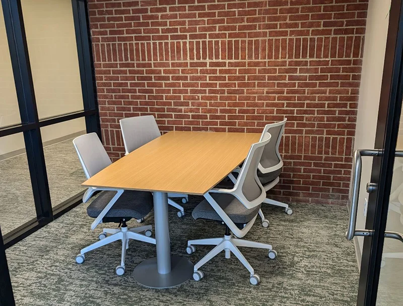 small room with table and empty chairs and brick wall in back